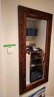 Full view of rectangular mirror mounted on wall with wooden mosaic block frame reflecting a small shoe rack and household items.