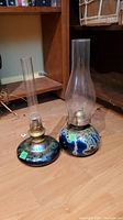 Two decorative glass oil lamps with iridescent multi-colored bases, brass burners, and clear glass chimneys.