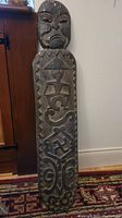 Full length photo of the carved wooden shield with tribal motifs showing face and geometric carvings.