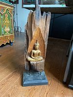 Front view of entire sculpture showing wooden slab, gold Buddha, metal stand, stone base