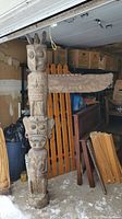 Full view of carved wooden totem pole with horizontal wing element leaning against it