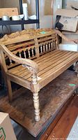 Front-left three-quarter view of the wooden bench showing carved backrest and slatted seat