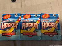 Three unopened 1991-92 OPC hockey wax trading card packs laid flat, showing front of each wax pack with OPC logo and 1991-92 season branding.