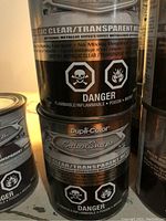 Three stacked cans of Dupli-Color Prism Metallic Clear Coat spray paint showing hazard labels and branding.