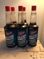 Five clear bottles of Red Line Two-Stroke Smokeless oil, each with a red cap, displayed on a worn wooden surface.
