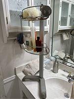 Metal bath caddy mounted on the side of a sink with bath products and a loofah sponge placed on it.