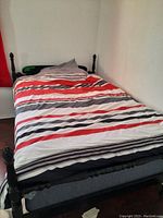 Full sized bed with black wooden frame and mattress, bedding includes striped and plain fabrics.