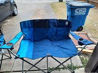 Blue folding camp loveseat with two cup holders on the armrests. Metal frame with blue fabric seat and backrest.