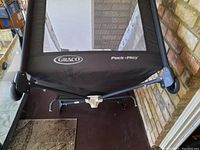 Photo of bottom part of a black Graco Pack 'n Play portable play yard showing brand and product line on mesh sides.