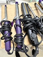 Curling irons with purple handles and flat iron with black and gold plates, cords wrapped around
