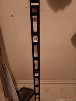 Photo showing a 3-foot black spirit level with bubble vials against a wall and floor