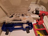 Red Black & Decker cordless drill with two plastic organizers containing various screwdriver bits on top of blue toolbox.