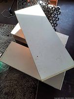Two white rectangular flat shelves stacked with some wear and marks visible