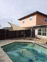 Wide view of beige triangular sun shade stretched over pool area, mounted to fence and house.