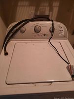 Front view of a white Whirlpool top load washing machine with control knobs and hoses on top.
