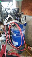Frontal view of blue vertical Campbell Hausfeld air compressor with attached red hose and black motor assembly