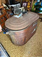 Copper boiler wash tub with fitted lid and black handles, showing antique wear and patina.