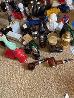 Photo showing multiple vintage Avon collectible bottles arranged on floor, including a red fire hydrant, green truck, blue eagle, brown pipe bottles, a black boot, a white bust, and other shapes.
