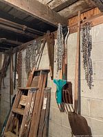 Garage wall featuring hanging metal chains in black and rusted condition, rusty shovel, garden rake with green handle, and a hand saw showing wear.