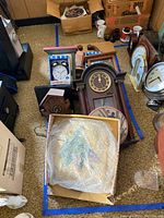 Overview of clocks including boxed Sharp alarm clock, wooden cuckoo clock, mantel clocks, and novelty milk can style clock. Items arranged on carpet floor.