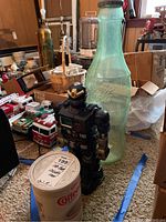 Photo showing tall frosted Coca-Cola bottle coin bank, vintage coffee can filled with marbles, and black robot toy.