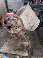 Full view of the concrete mixer showing the drum, metal frame, and gear wheel with visible rust and dirt.