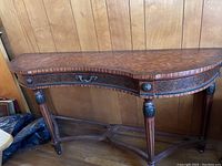 Front view of the wood demilune console table showing its curved top and detailed carved legs against a wood panel wall.