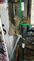 Photo showing large metal crowbars, vintage log saw blades leaning against wall, worn leather/canvas tool belts hanging