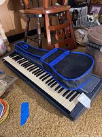 Yamaha PSR-240 electric keyboard side view with black Mark II guitar and soft guitar case on top.