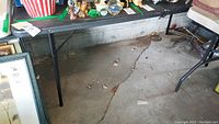 Full view of metal folding table with contents on top and concrete garage floor beneath