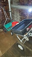Photo showing both spreaders: the Agri-Fab Broadcast Spreader 100 with black plastic spreader box and the Sears green bucket style spreader, with a red bucket between them