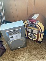Photo showing YORX speaker and Spirit of St. Louis mini jukebox side by side on a carpeted floor in front of wood panel wall.