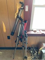 Two telescopes mounted on tripods shown against wood-paneled wall and window, focusing on general lot contents and stands.