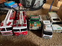 Six toy trucks arranged on carpet, two red Tonka fire trucks with ladders, and four Hess trucks in white, green, and black color schemes.