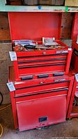 Stacked red tool chests: top chest hinged open showing interior contents, bottom rolling cabinet visible