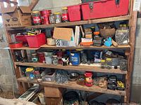 Wide view of wooden shelving with plastic crates, jars, metal bowls, and assorted hardware and tools arranged on shelves.