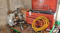 Red metal tool chest with drawers, yellow extension cord on top, assorted hand tools scattered around, and Craftsman bench grinder visible beside the chest.