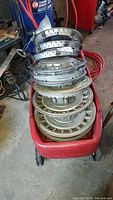 Stack of various metal hub caps including some smooth and traditional designs, inside a red Radio Flyer wagon.