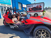 Red Polaris Slingshot three-wheeled autocycle parked outside rental shop with two passengers wearing helmets