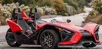 Front-side view of red Polaris Slingshot autocycle on paved road with landscaped background