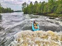 Group raft navigating a rapid section of the Ottawa River surrounded by forest