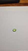 Oval cut apple green Peridot gemstone on white background, showing top view of facet cuts and clarity.