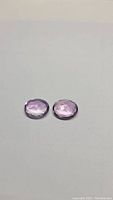Close-up of the two oval cut light pink-purple amethyst gemstones, showing faceted surfaces and color.