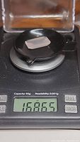 Photo shows the soft pink emerald cut stone placed on a black round platform with a digital scale displaying weight 16.865 carats.