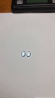 Two small pear-shaped natural sky blue topaz gemstones placed on a white background, showing the front and back views of the stones.