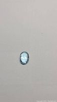 Top view of the oval cut blue topaz gemstone showing polished domed face and blue hue.