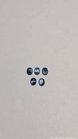 Five teal oval untreated kyanite gemstones laid out in two rows against a plain background
