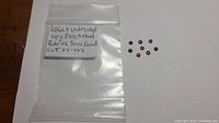 Plastic bag with handwritten label listing details: 1.06ct untreated, very rare natural rubies, 3mm round cut VS-VVS clarity. Eight small deep red round cut rubies positioned beside the bag.