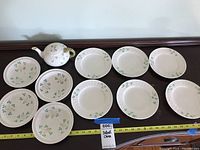 Full view of Belleek Irish China set showing 6 plates, 4 bowls, and the small teapot laid out on a surface with a measuring tape indicating size.