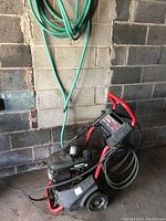 Photo of the Excell gas power washer leaning against a concrete block wall with hose coiled above it.